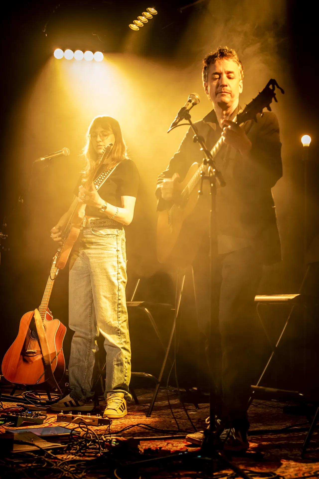 Deux musiciens debout au micro, silhouettes découpées dans un halo doré et brumeux.