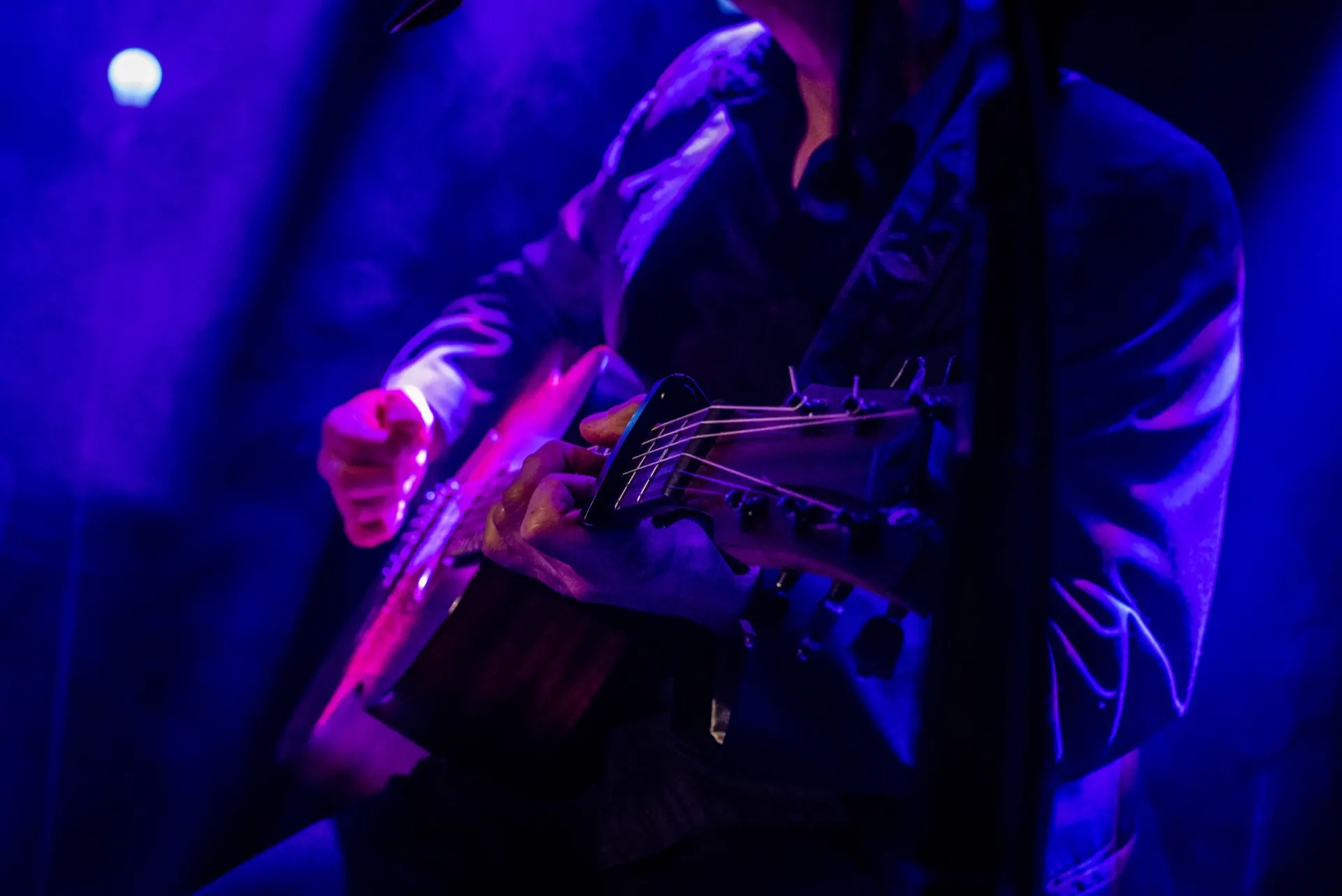Détail du buste et des mains sur une guitare, reflets bleus et violets.