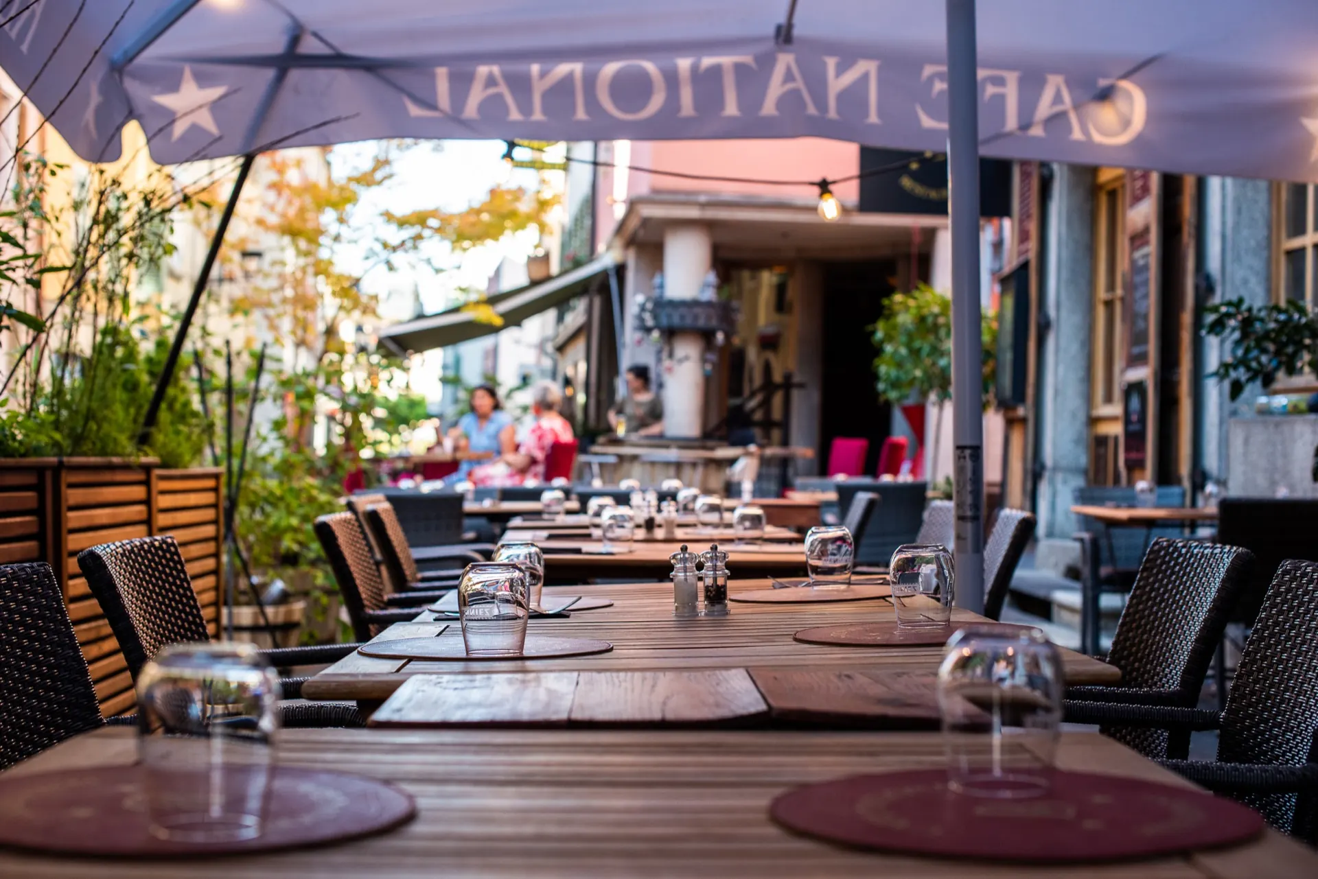 Longue table dressée sous un parasol, terrasse du Café National en fin de journée